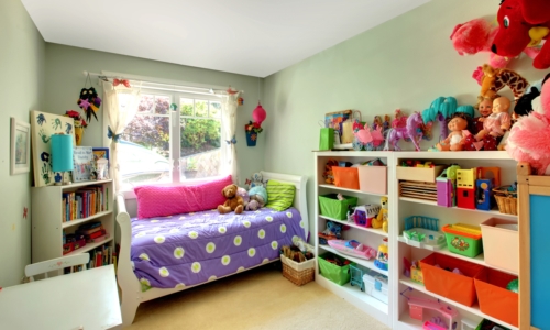 Girls bedroom with many toys and purple bed.