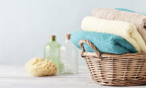 Bath towels of different colors in wicker basket on light background