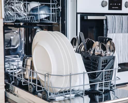 Open dishwasher with white clean dishes after washing in modern scandinavian kitchen. Clean kitchenware in open dishwashing machine.