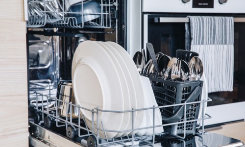 Open dishwasher with white clean dishes after washing in modern scandinavian kitchen. Clean kitchenware in open dishwashing machine.