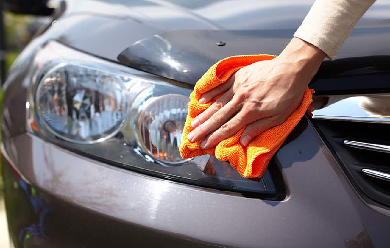 Hand with microfiber cloth cleaning car headlight covers.