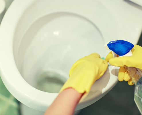 gloved hands cleaning a toilet bowl
