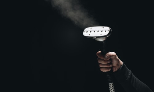 cropped shot of male holding garment steamer with steam on black