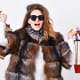Woman shopping luxury boutique. Girl wear sunglasses and fur coat shopping white background. Lady hold shopping bags. Discount and sale. Buy with discount on black friday. Shopping with promo code.