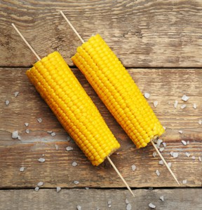 Boiled corn on sticks with salt on wooden background