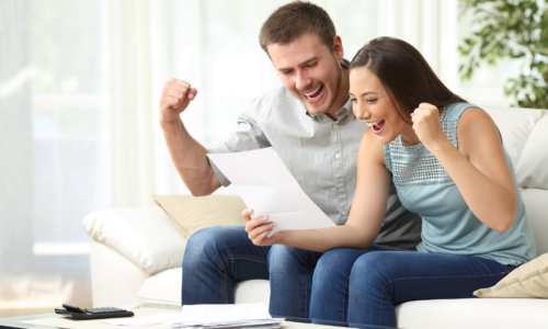 Excited couple seeing their tax refund status sitting on a sofa in the living room at home