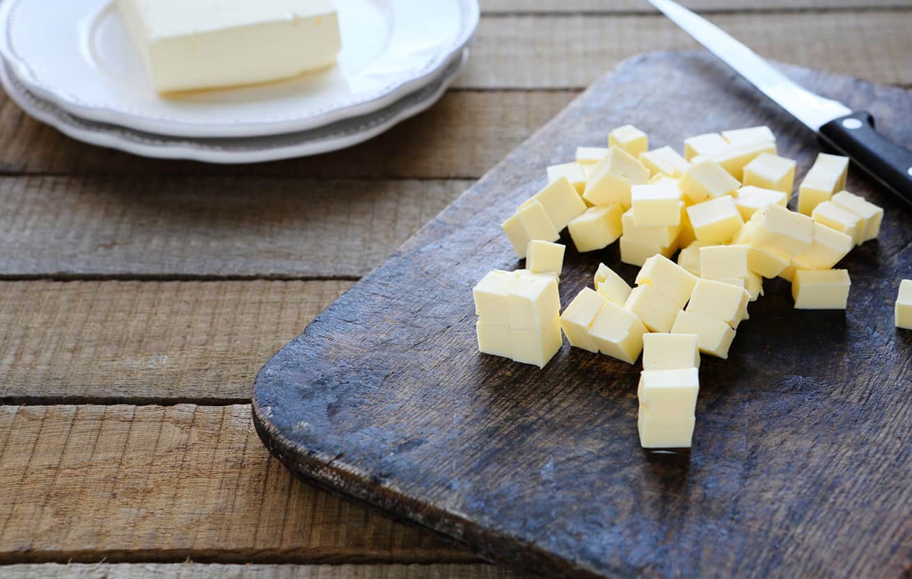 butter along side a knife that has cut it into small pieces sitting on a black cutting board