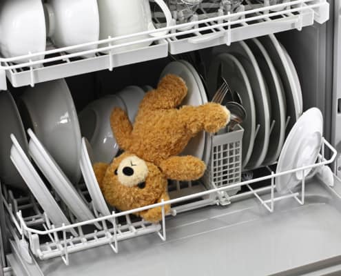 dishwasher holding toy bear with white dishes