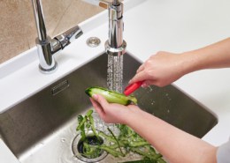 Cropped view of female hands peeling cucumber over Food waste disposer machine