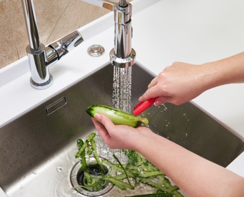 Cropped view of female hands peeling cucumber over Food waste disposer machine