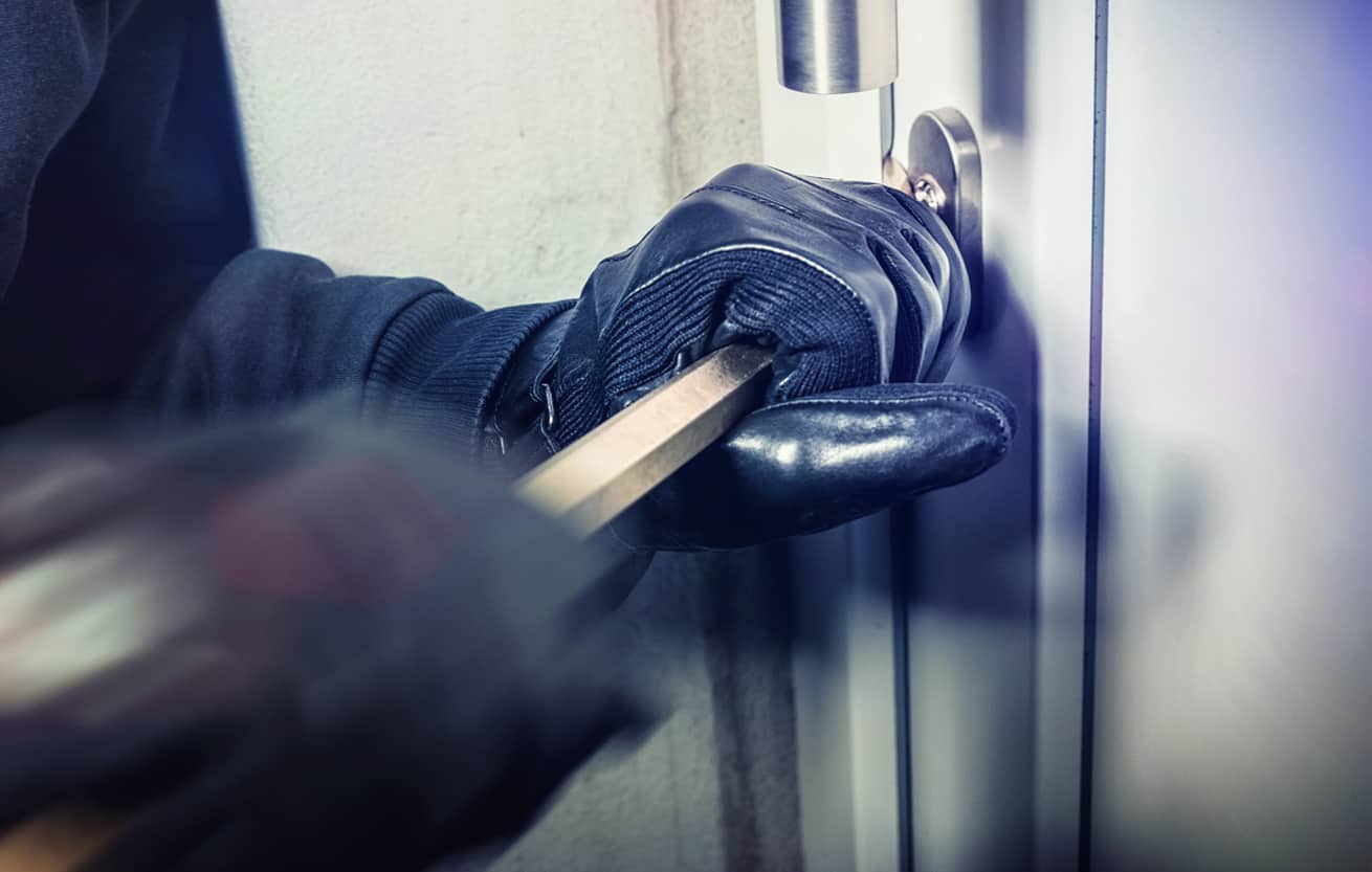 gloved hands of burglar using crow bar to break into a home