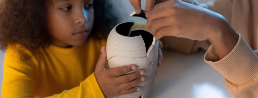 young girl getting help with gluing back together a broken white vase