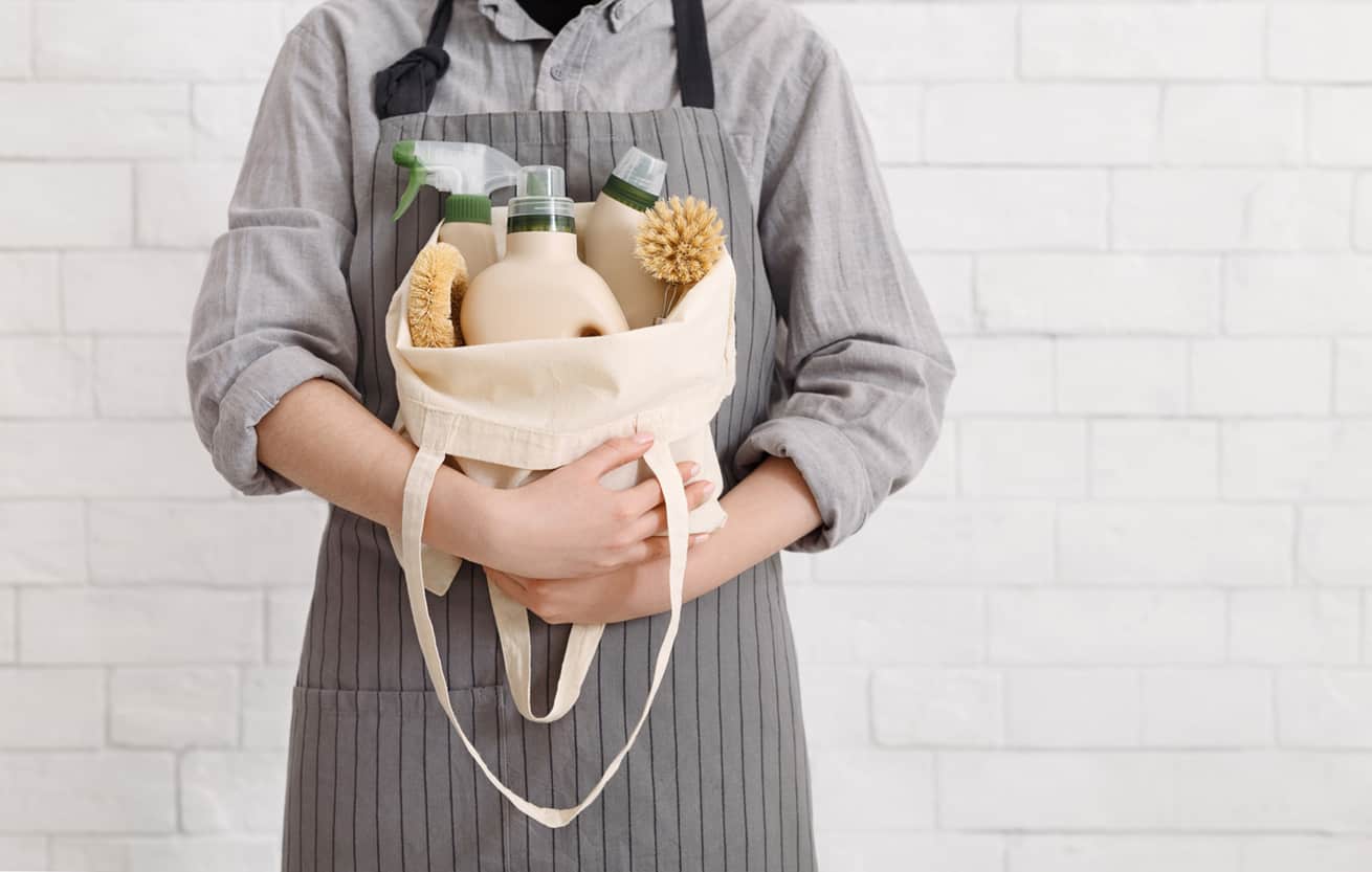 woman wearing apron holding a beige linen bag filled with her homemade cleaners