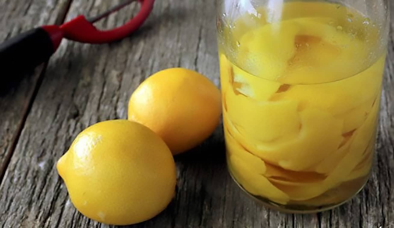homemade lemon extract in jar on wood table with fresh lemons on the side