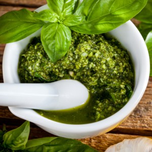Homemade pesto sauce with basil and pine nuts in white mortar over old wooden table