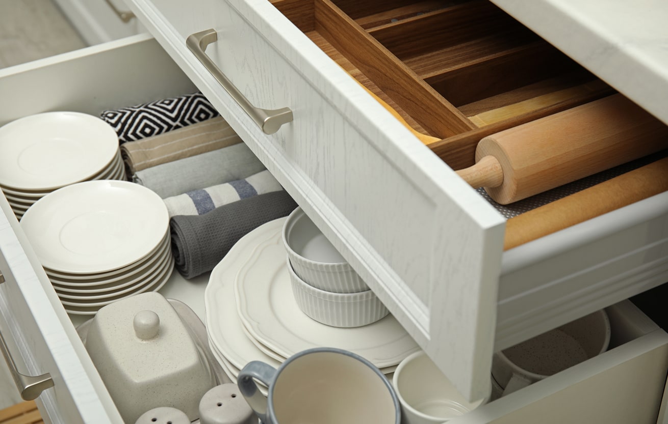 Open drawers of kitchen cabinet with different dishware, utensil