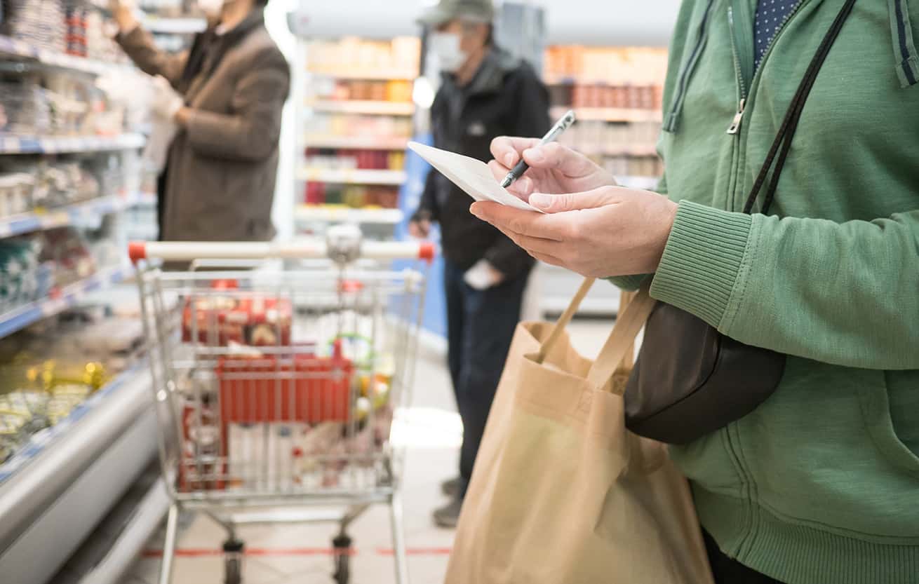Woman with a shopping list at a grocery store with people shopping in the background