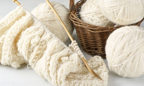 Natural woolen yarn and knitting on vintage wooden background.