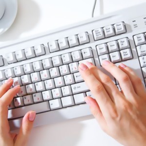 female hands typing on white computer keyboard on white desk