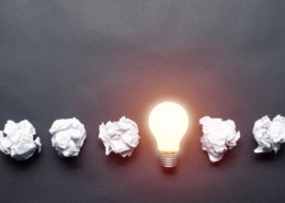 Lightbulb and crumpled white paper balls on black background. Successful solution of problem. Think outside the box. Business motivation with copy space. Genius idea among failing ideas metaphor.