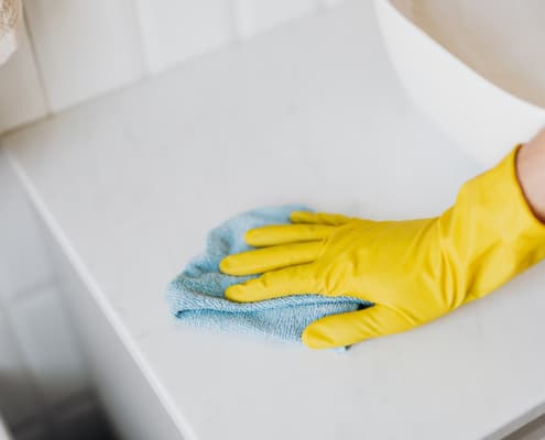 rubber gloved hand cleaning white surface with a blue microfiber cloth