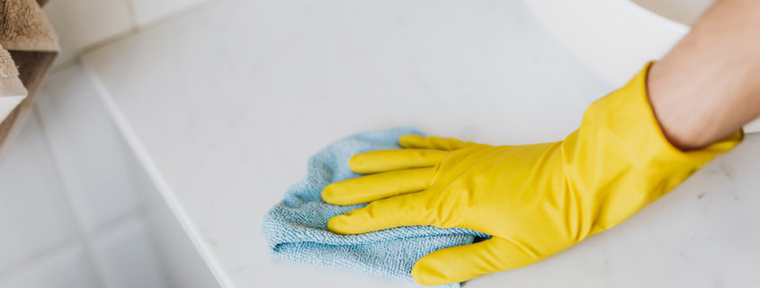 rubber gloved hand cleaning white surface with a blue microfiber cloth