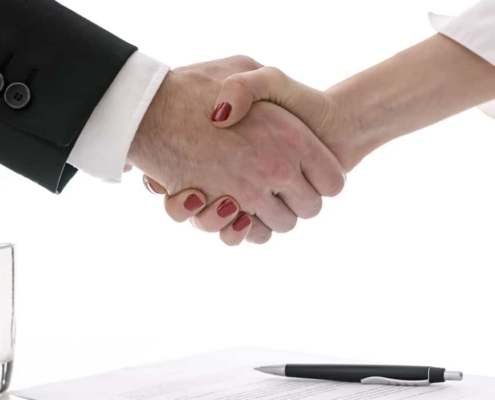 Man and woman shaking hands above table having negotiated a signed contract.