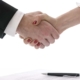 Man and woman shaking hands above table having negotiated a signed contract.