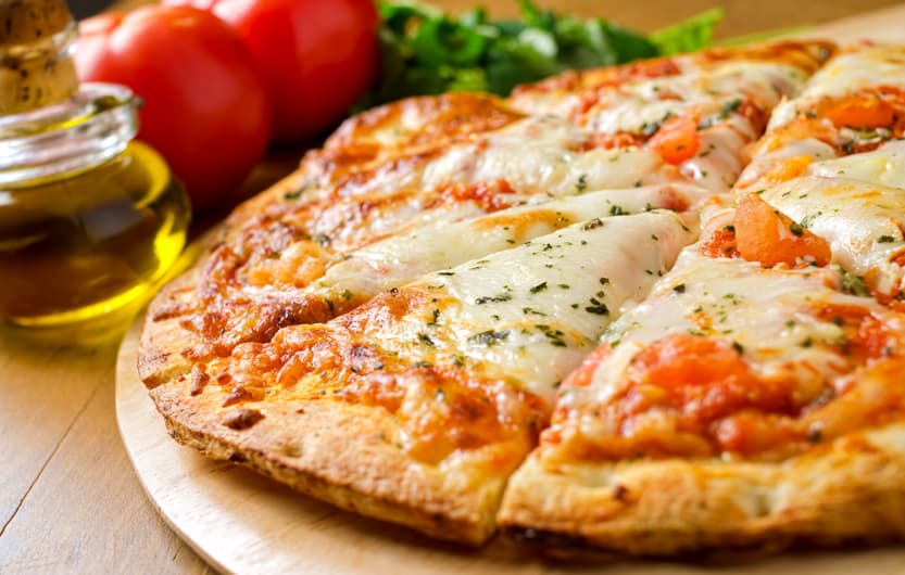 A freshly baked pizza margherita with olive oil, tomatoes, fresh basil, and mozzarella cheese.