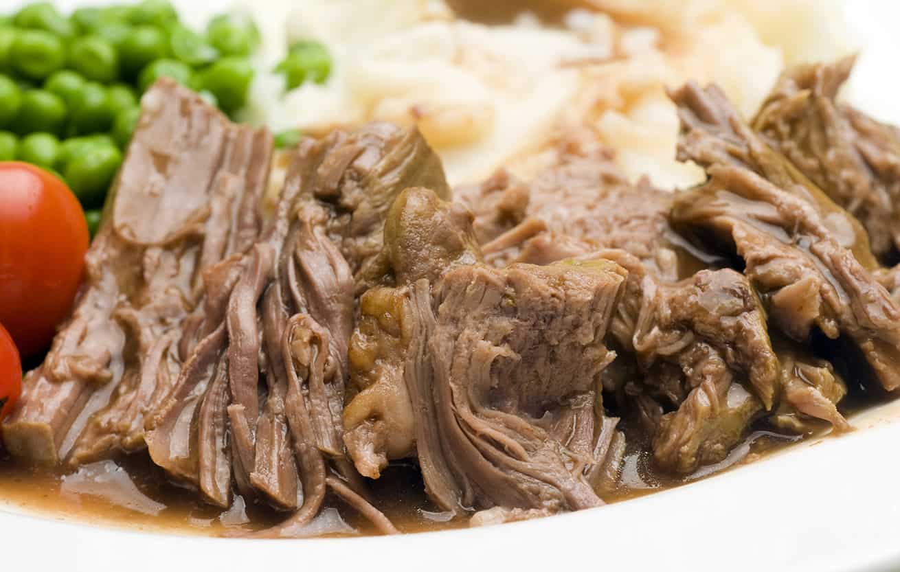 sliced pot roast beef dinner with peas mashed potatoes and gravy