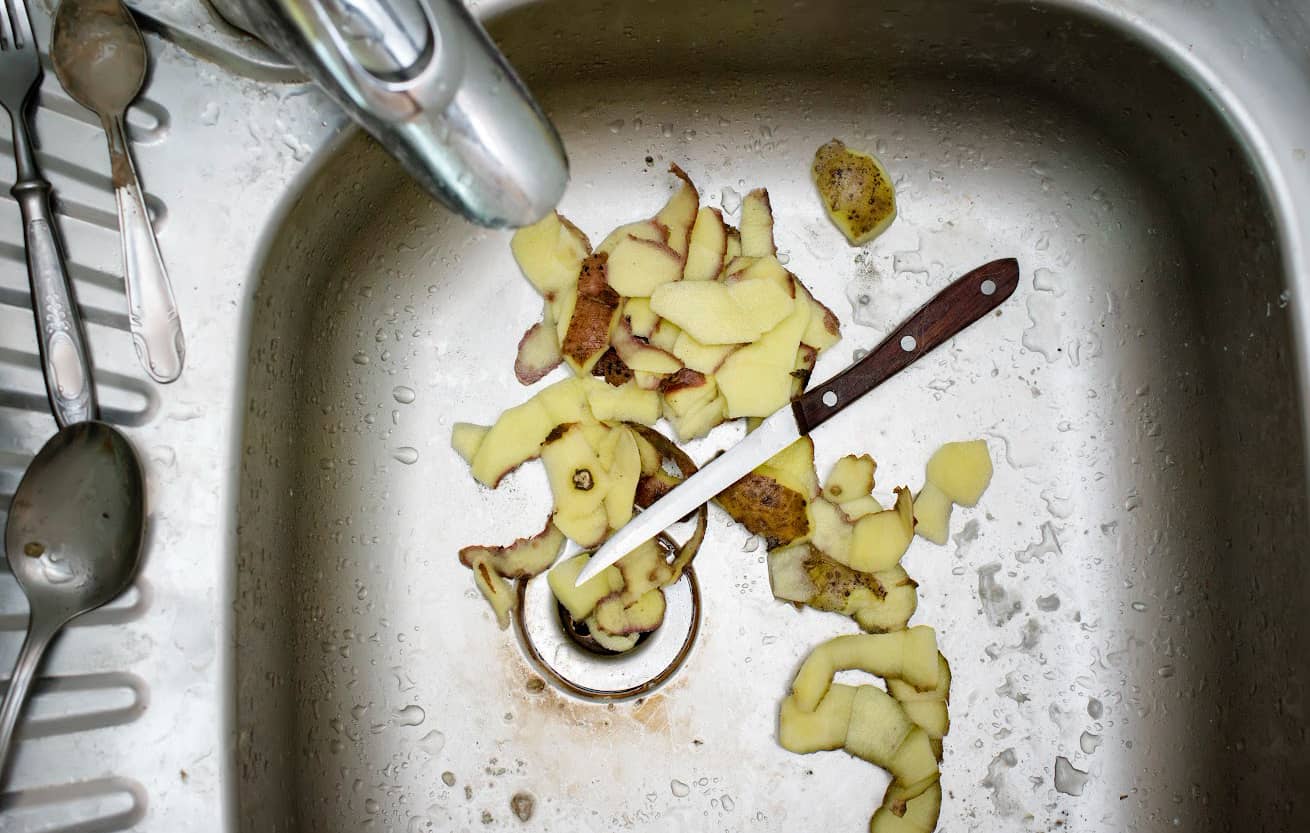 Leftovers and peeled potato skin with a kitchen knife left in a kitchen sink, overhead indoors shot