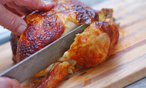Closeup of a man slicing into a rotisserie chicken leg