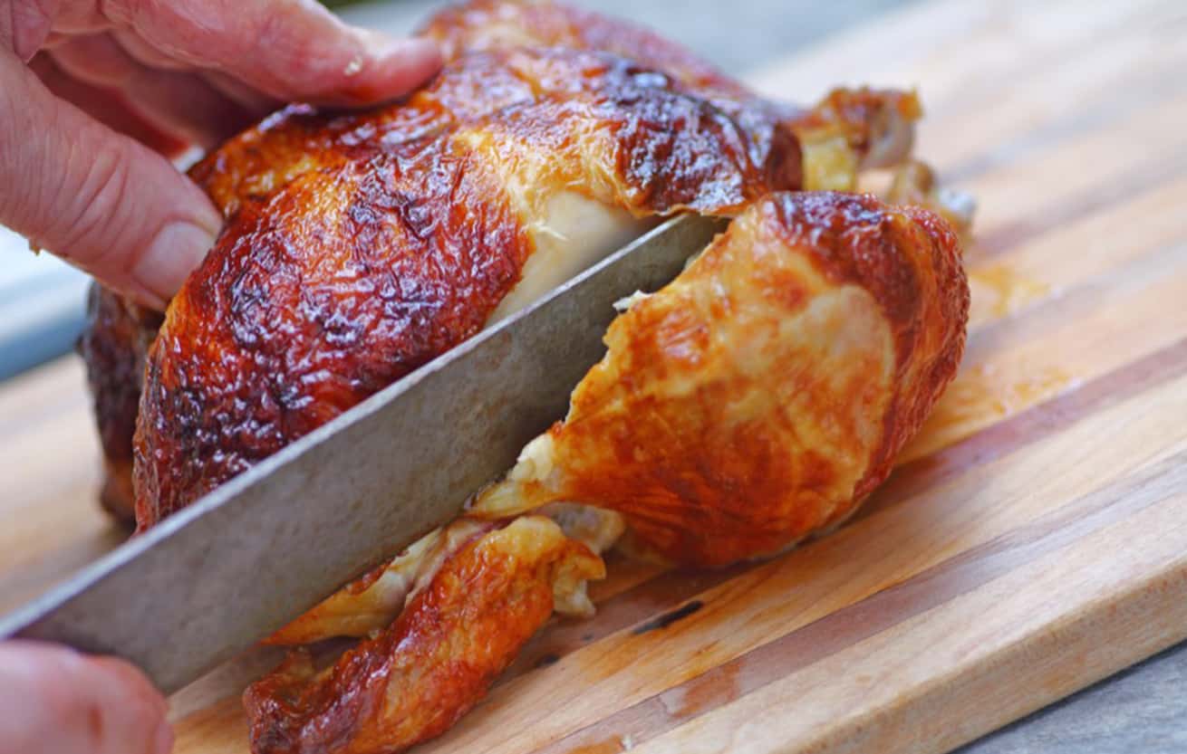 Closeup of a man slicing into a rotisserie chicken leg