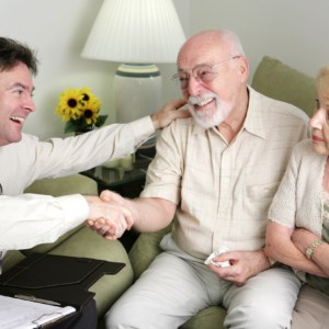 A married senior couple seeing a home equity scam artist. The men have reached and agreement and the wife looks angry.
