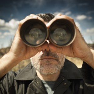 Man with binoculars in a field looking for money