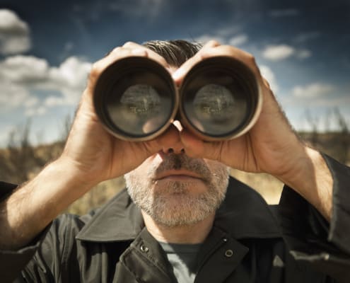 Man with binoculars in a field looking for money