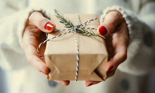 female hands holding small brown paper wrapped gift with sprig of fresh greenery