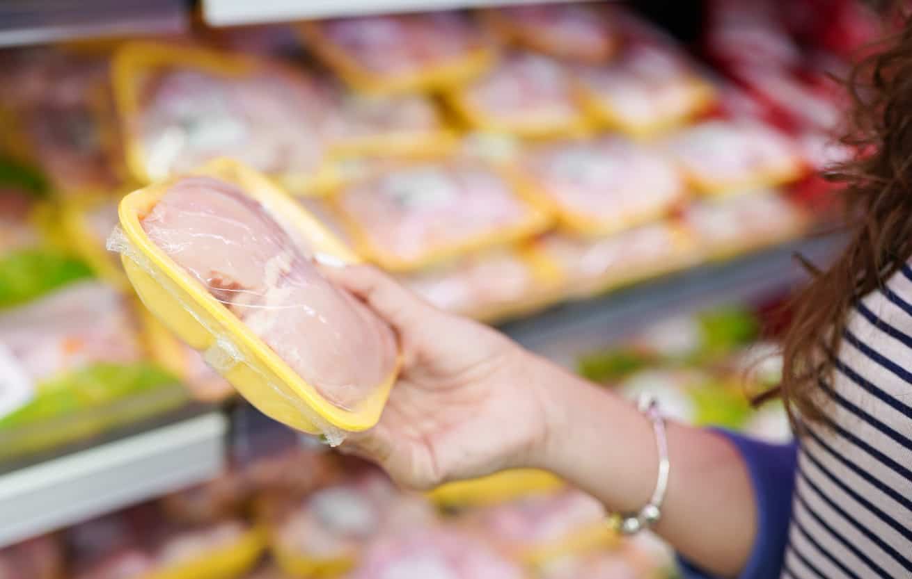 meat in food store . Woman choosing packed fresh chicken meat in supermarket .