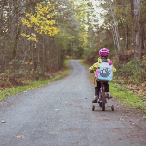 preschool girl on bike with training wheels on a country path on her way to school