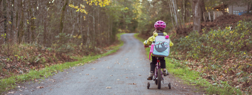 preschool girl on bike with training wheels on a country path on her way to school