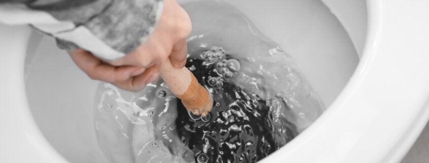 male hands holding plunger to unclog toilet