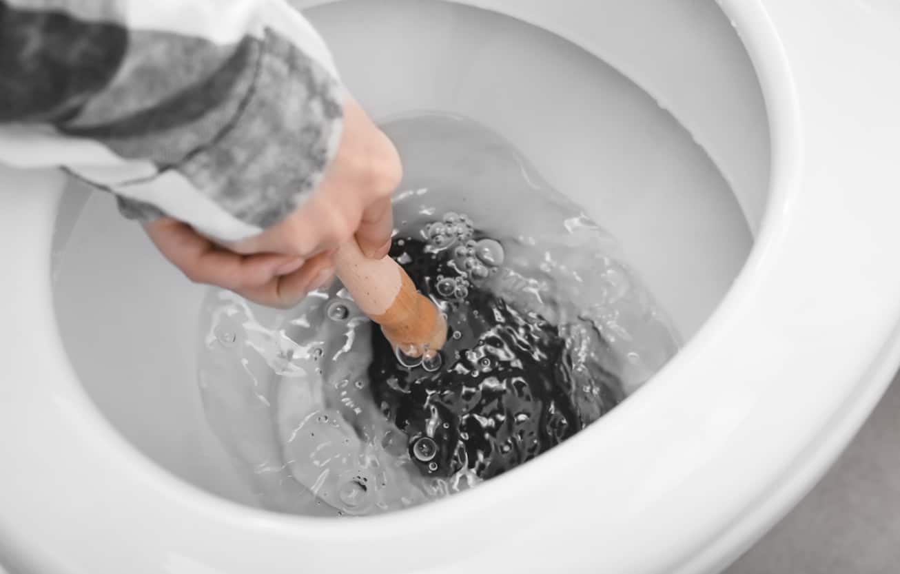 male hands holding plunger to unclog toilet