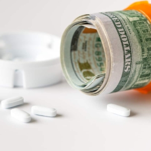 Healthcare cost concept using US Dollars with white medicine pills spilling from medicine bottle.