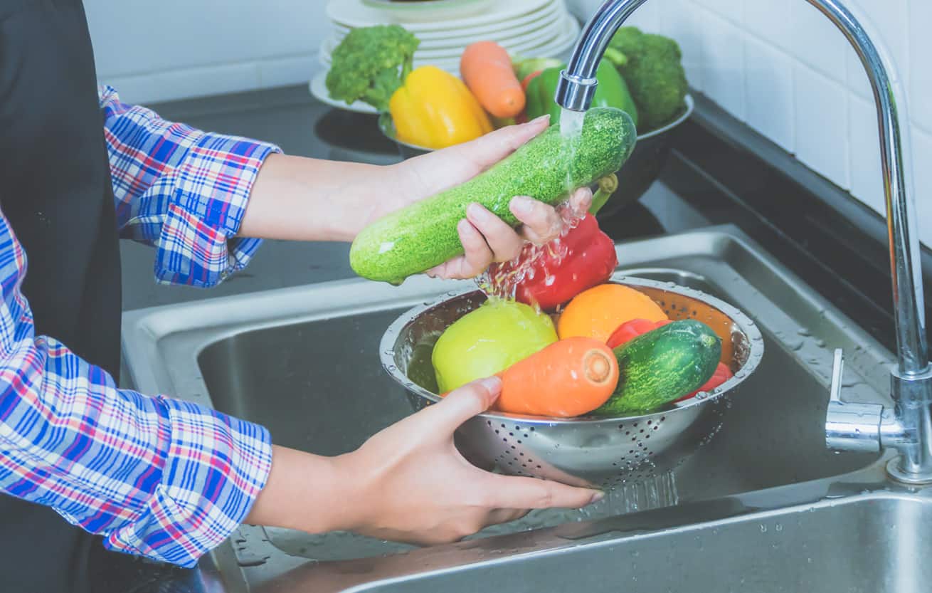 Woman washing produce in kitchen sink