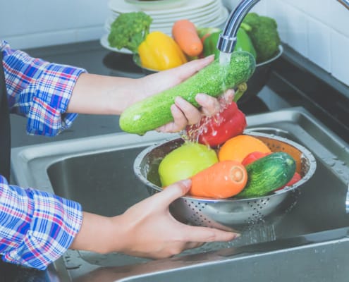 Woman washing produce in kitchen sink