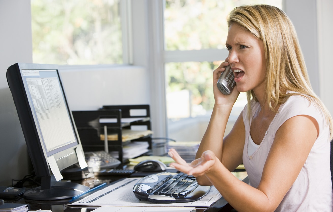 Woman in home office with computer using telephone frowning 