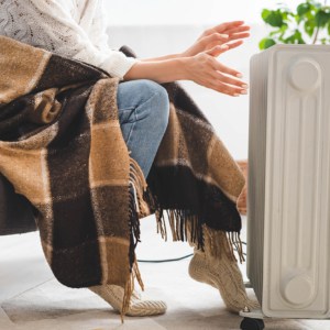 cropped view of girl with blanket warming up with heater in cold room