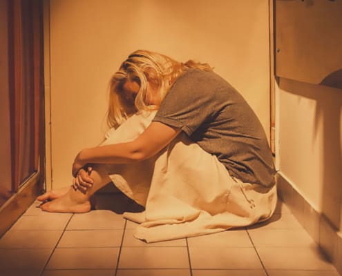 ad, depressed and lonely woman sitting in a corner on a floor tiles, in a skirt, barefoot with a long blond hair