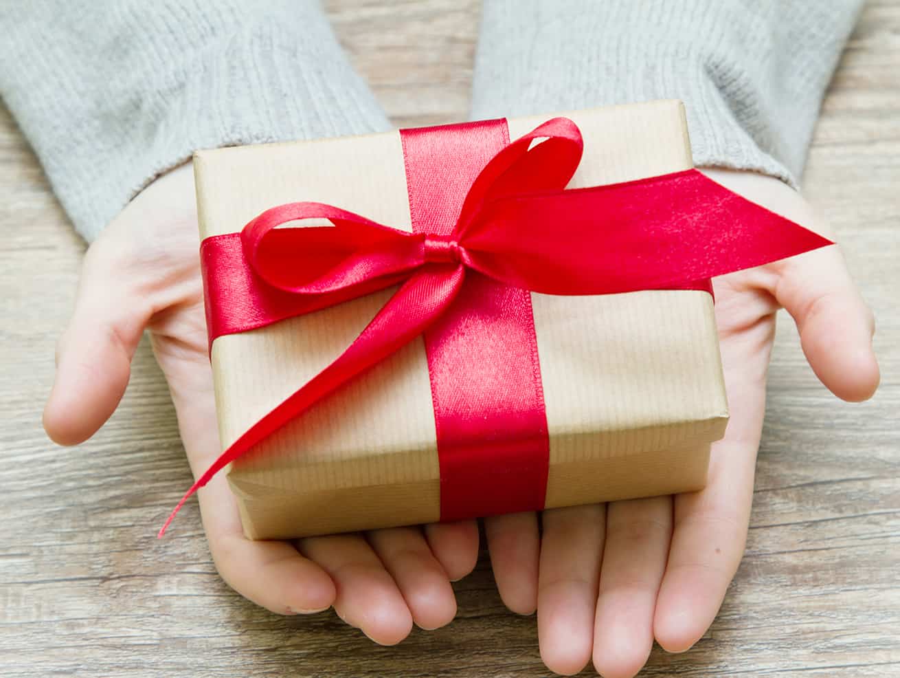 hands holding small Christmas gift in kraft paper and red bow
