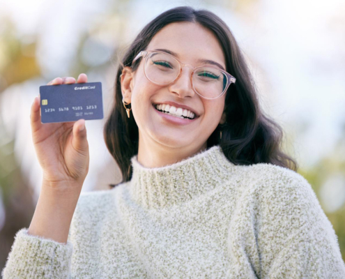 a happy young woman holding up a credit card while standing outside.